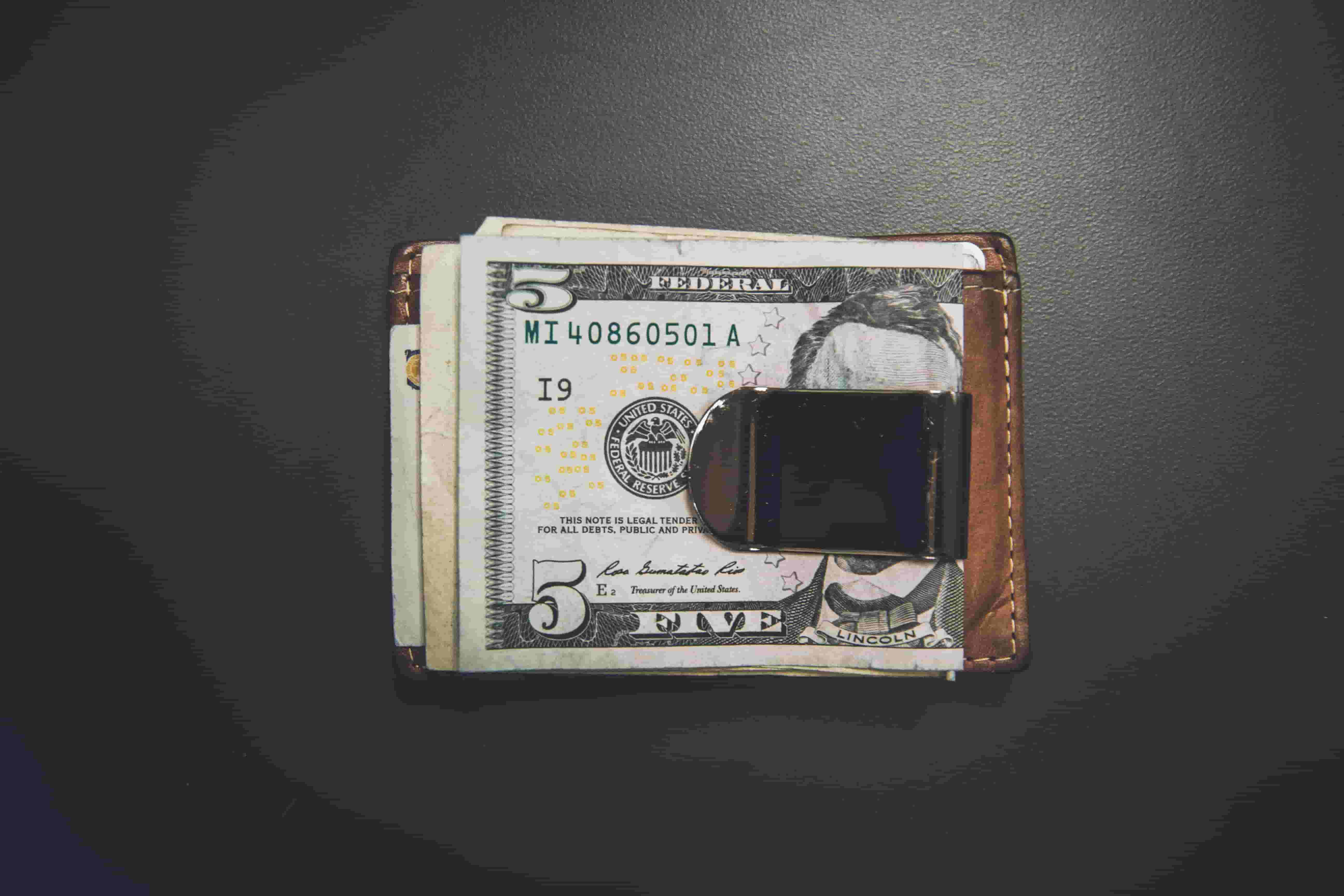 A folded five dollar bill clipped to a brown wallet A folded five dollar bill clipped to a brown wallet